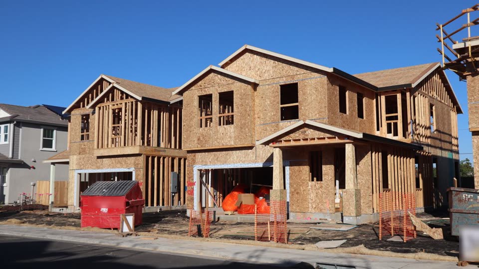 A new two-story home being framed in a subdivision, next to finished new homes
